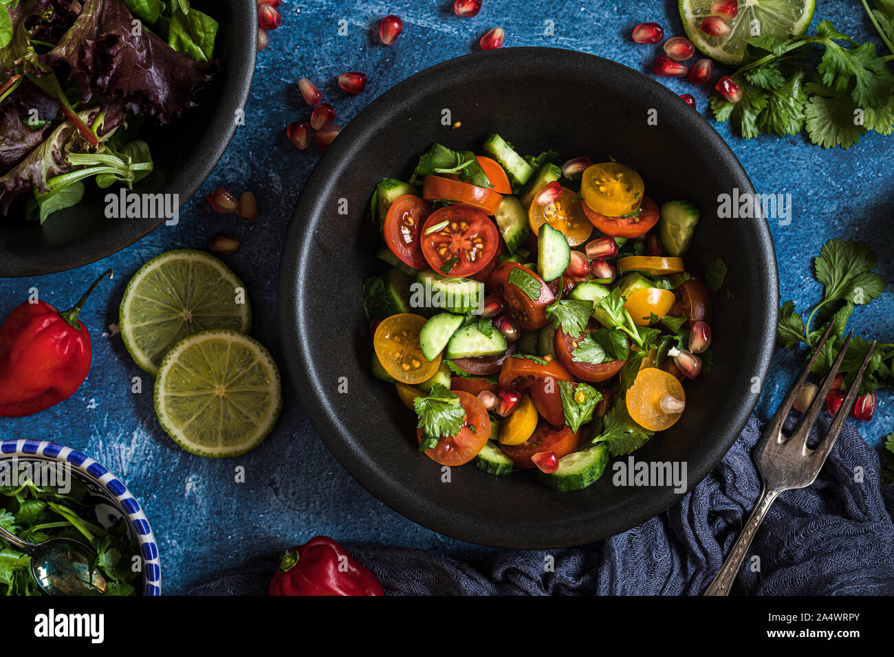 Fresh salad with tomato, cucumber and herbs, flat lay from above  The salad is in a black bowl and there are other bowls with ingredients around it. T Stock Photo