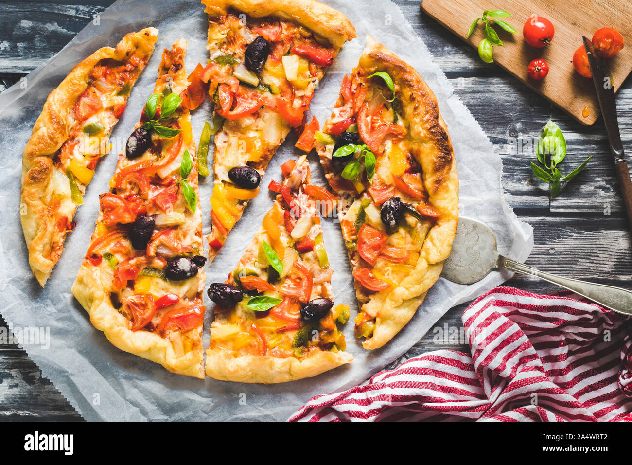 Homemade pizza with vegetables on a dark background. The pizza is cut in pieces in irregular size and is viewed from above.  With a red and white napk Stock Photo