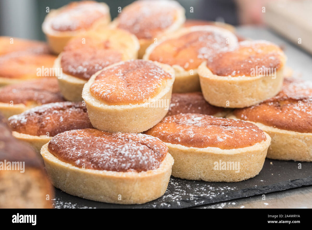Swedish traditional pie mazarin tart filled with almond paste. The tarts are piled up on a black background and are sprinkled with icing sugar. Stock Photo