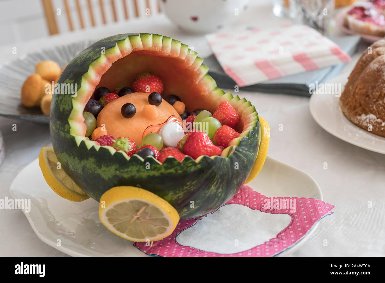 A baby in a baby carriage made out of fresh fruit. The carriage is made out of a watermelon. Served at baby shower, celebration of the new baby and mo Stock Photo
