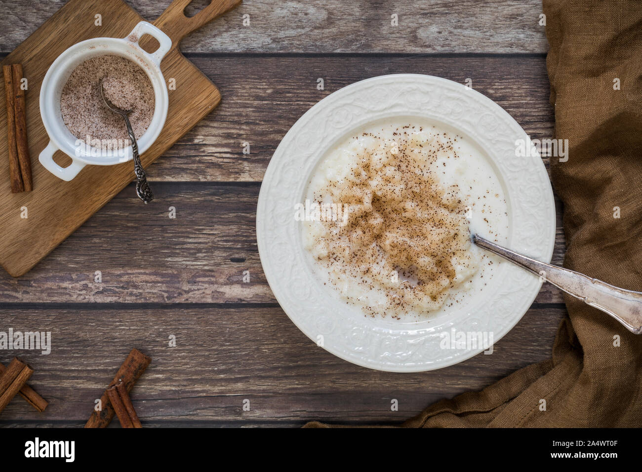 Traditional Swedish rice pudding with ground cinnamon flat lay from above perspective. There is a small bowl with cinnamon and sugar on a wooden board. Stock Photo