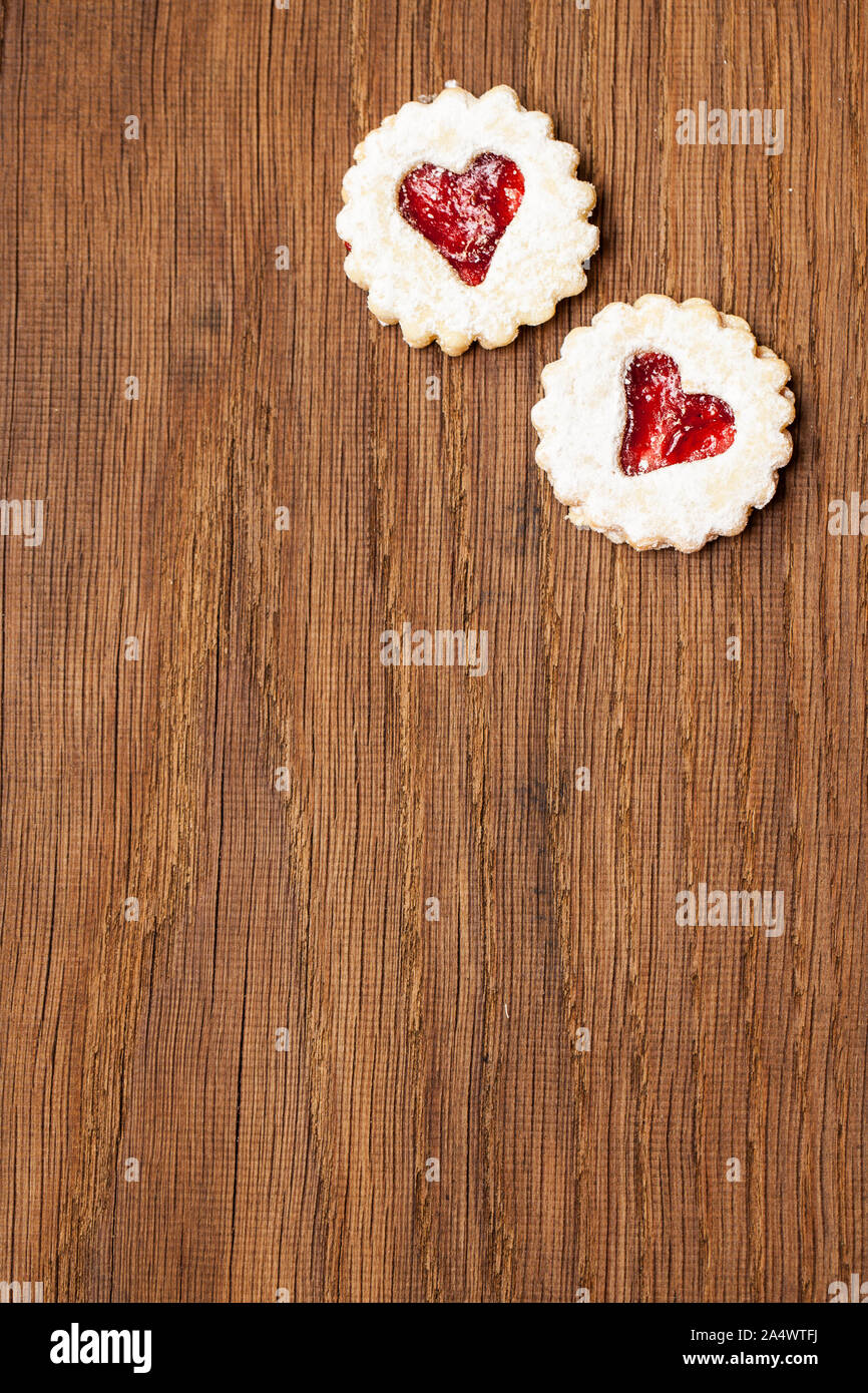 Two cookies filled with red jam with heart on wooden board Stock Photo