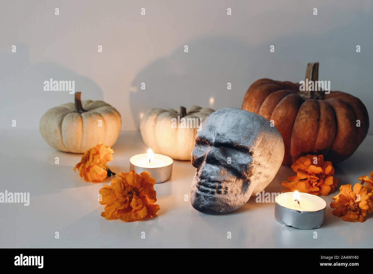 Dia de los Muertos, Mexican Day of the Dead table altar composition. Orange tagetes, marigold flowers and human artificial skull decoration. Burning Stock Photo