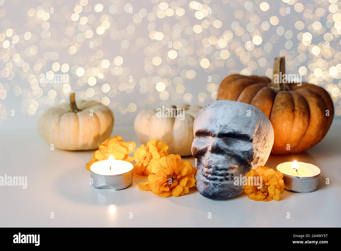 Dia de los Muertos, Mexican Day of the Dead table composition. Orange tagetes, marigold flowers and artificial skull decoration. Burning candles and Stock Photo