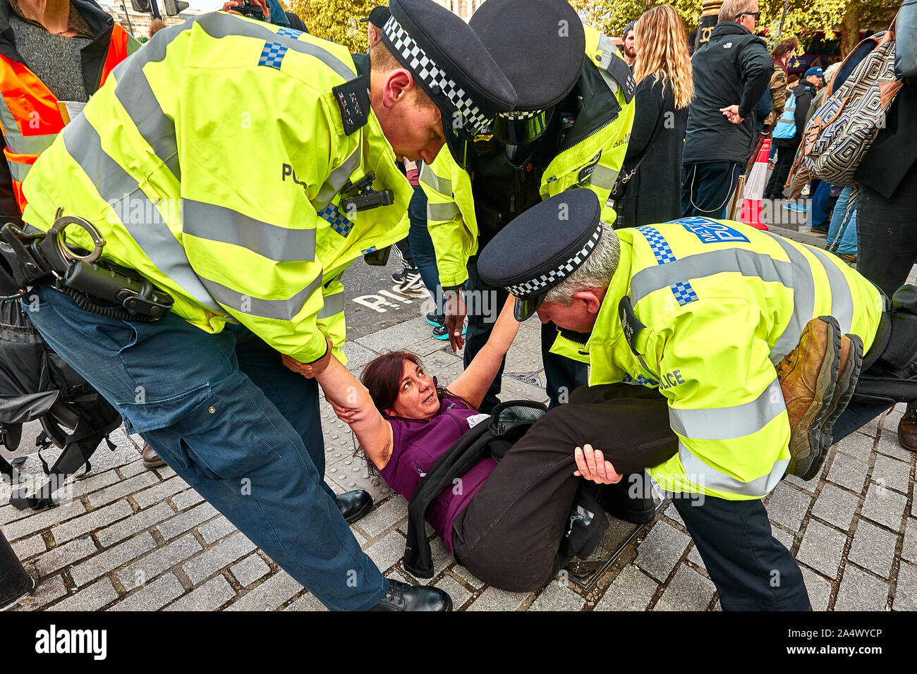 London, U.K. - Oct 16, 2019: An environmental campaigner from Extinction Rebellion is dragged away by Police after blocking watched on a road in Trafalgar Square. Stock Photo