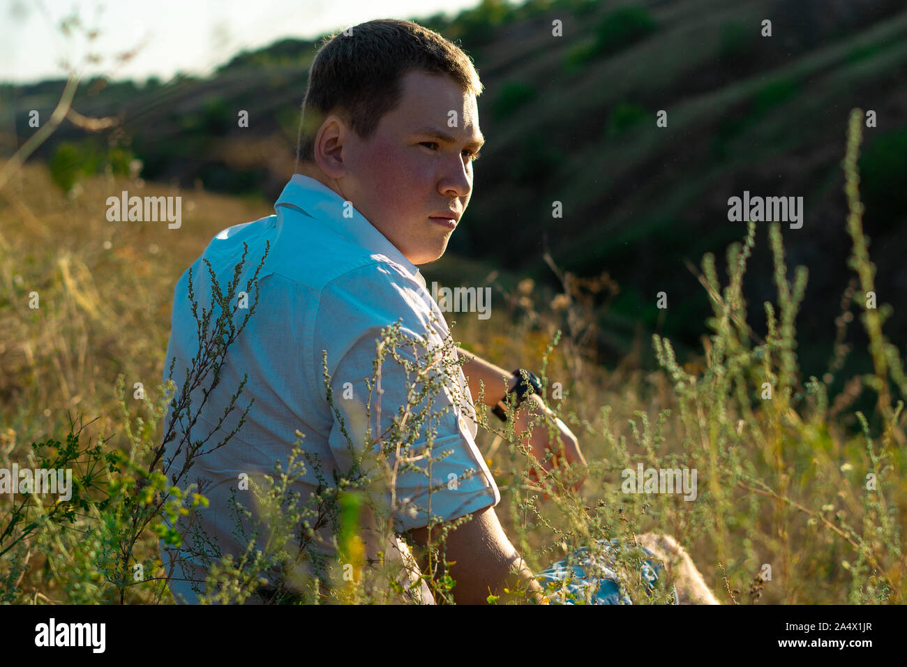 Beautiful portrait of handsome man sitting in field at sunset  Stock Photo