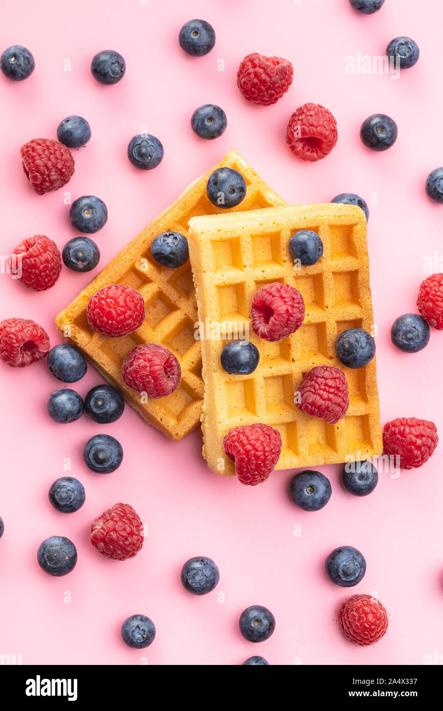 Waffles with blueberries and raspberries on pink background. Stock Photo