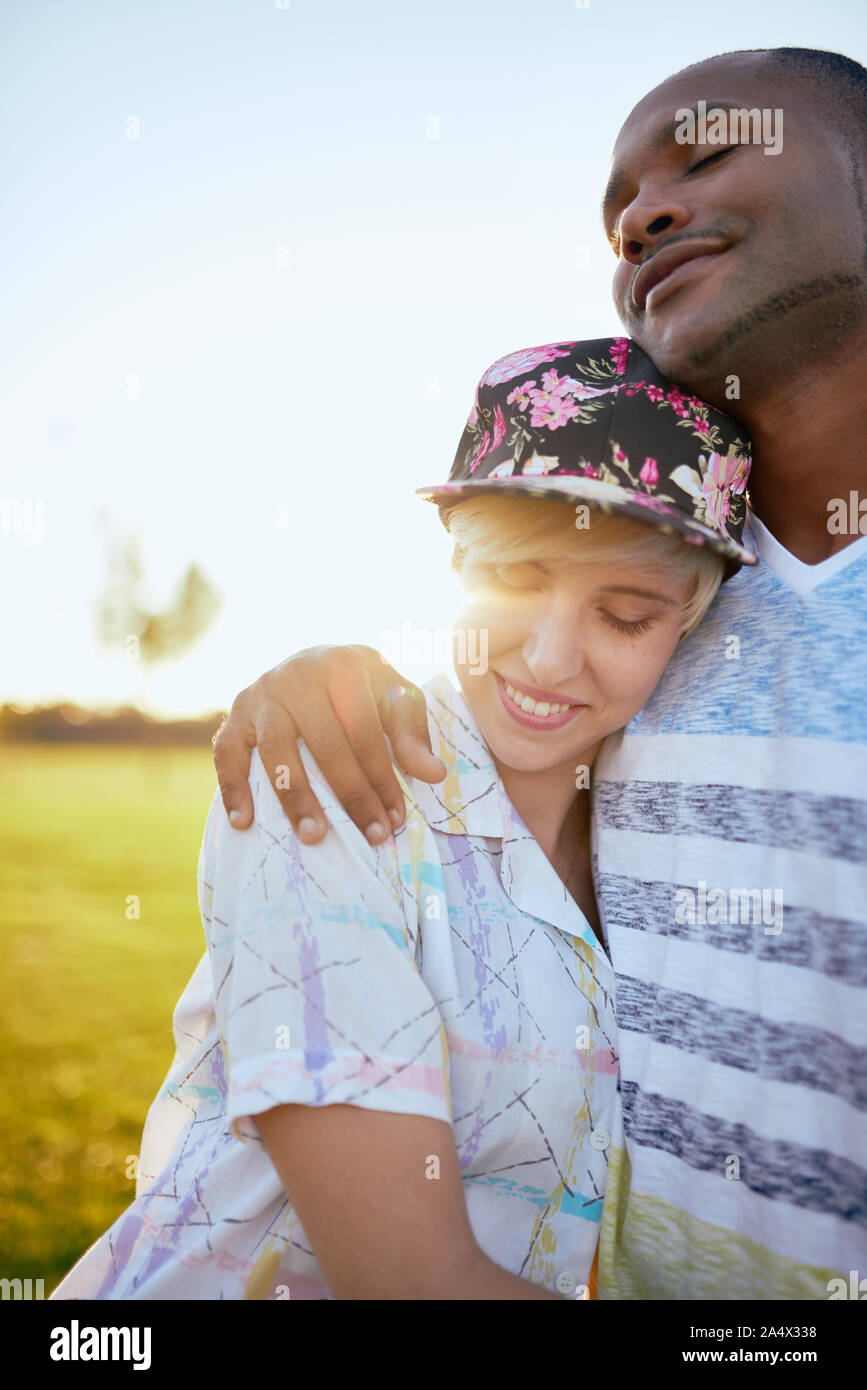 Mixed race couple of millennials in a grass field cuddling and s Stock Photo