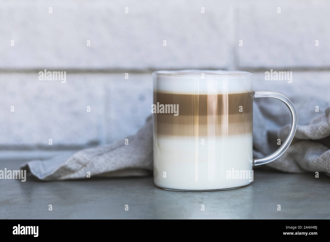 Coffee Cafe Latte Macchiato outdoors in a seethrough glass cup with a rustic gray tile background and a linen napkin. Side view with room for text. Stock Photo