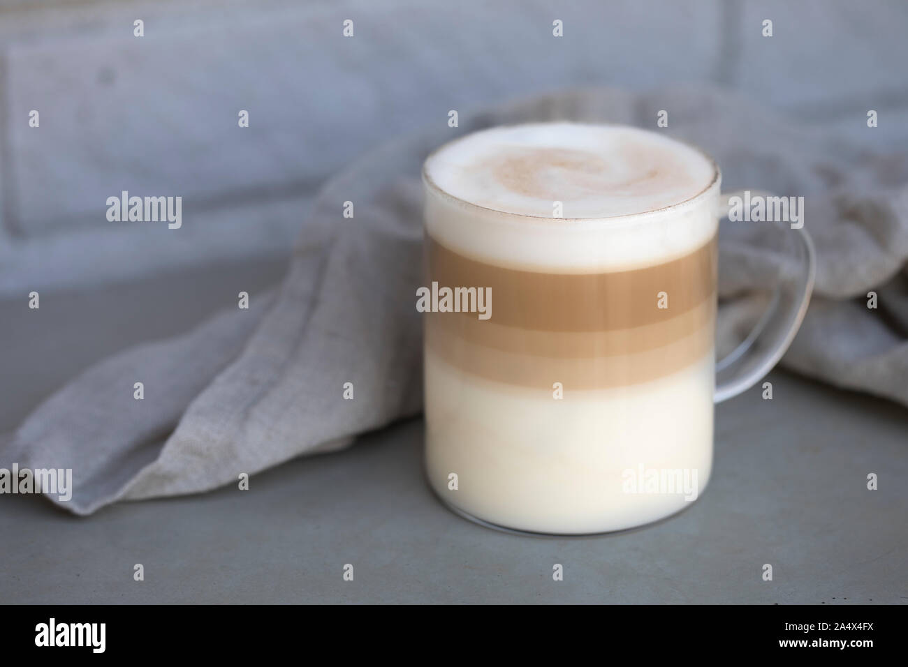 Coffee Latte macchiato outdoors in a seethrough glass cup. The cup is on a rustic concrete table with a gray background. Room for text in the photo. Stock Photo