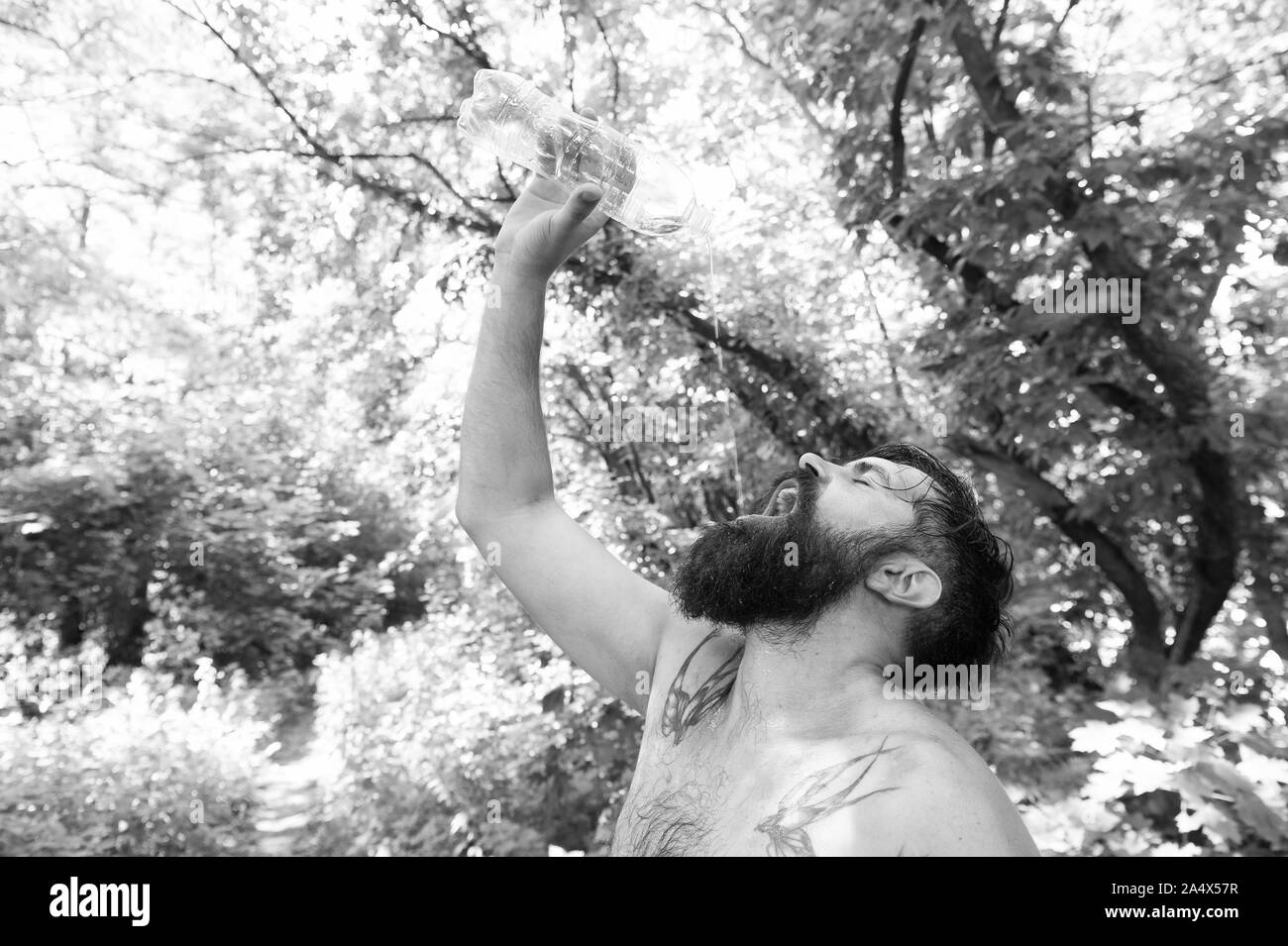 Water is life. Thirsty hipster drinking fresh water on hot summer day. Bearded man having a drink from water bottle on natural environment. Quenching thirst with natural mineral clean water. Stock Photo