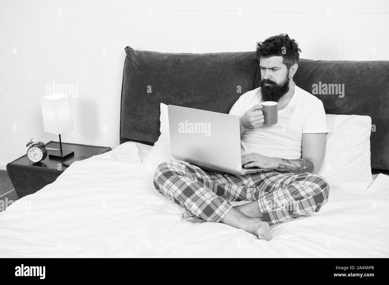 Just woke up and already at work. Hipster bearded guy pajamas freelance worker. Remote work concept. Social networks internet addiction. Online shopping. Man surfing internet or work online. Stock Photo
