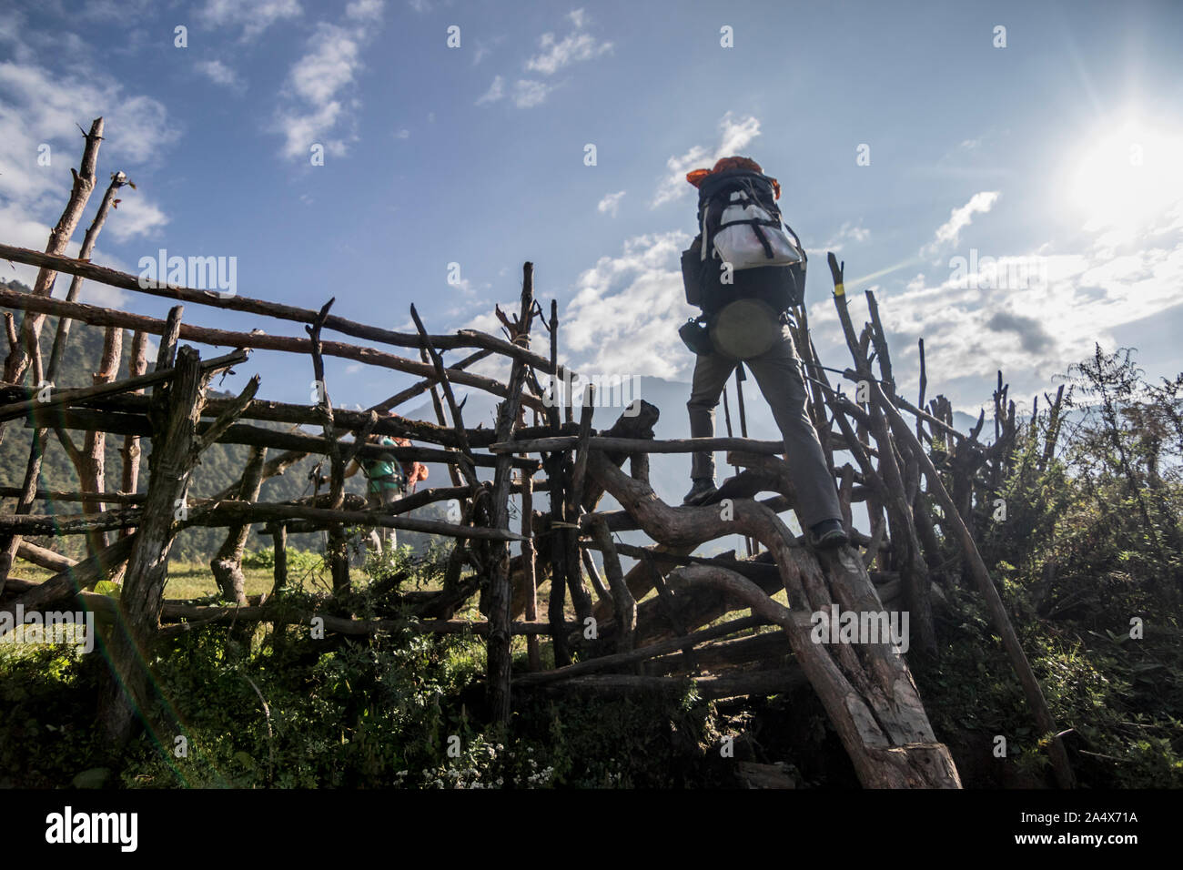 A trekker crosses a tattery fence in rural Nepal Stock Photo