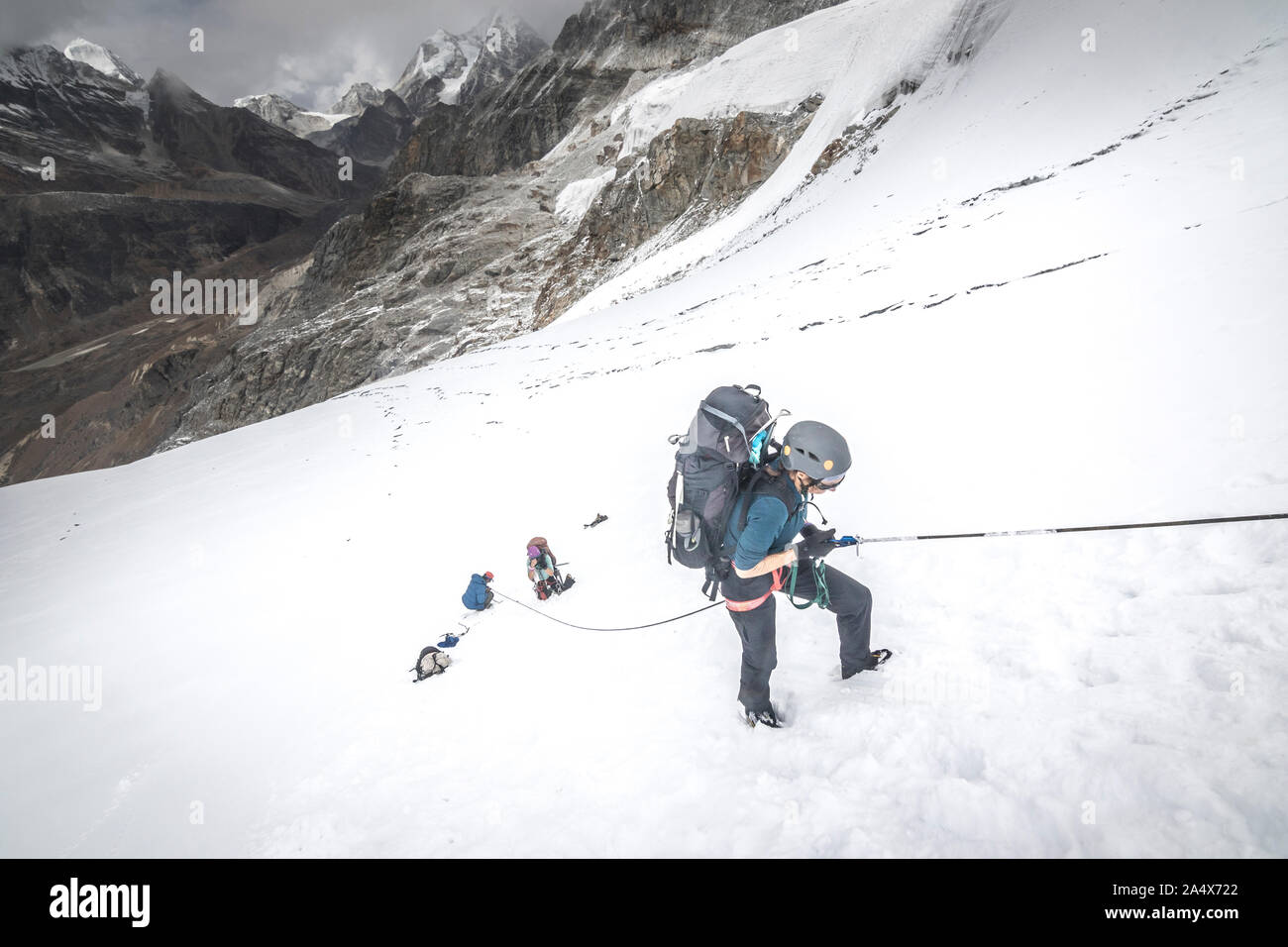 A woman climber ascends a fixed line on a steep snow slope Stock Photo