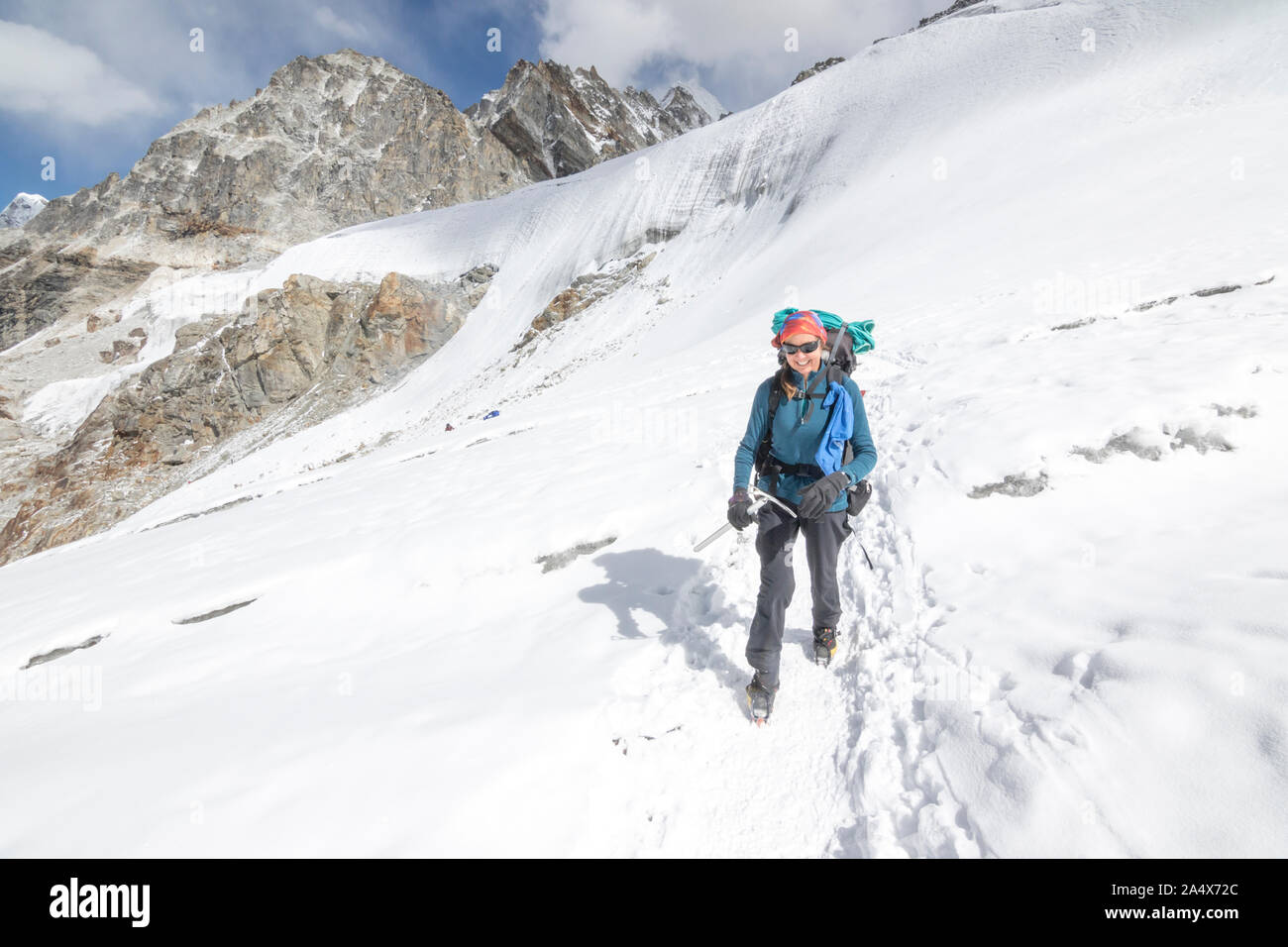 A woman mountaineer with ice axe smiles while crossing a glacier Stock Photo