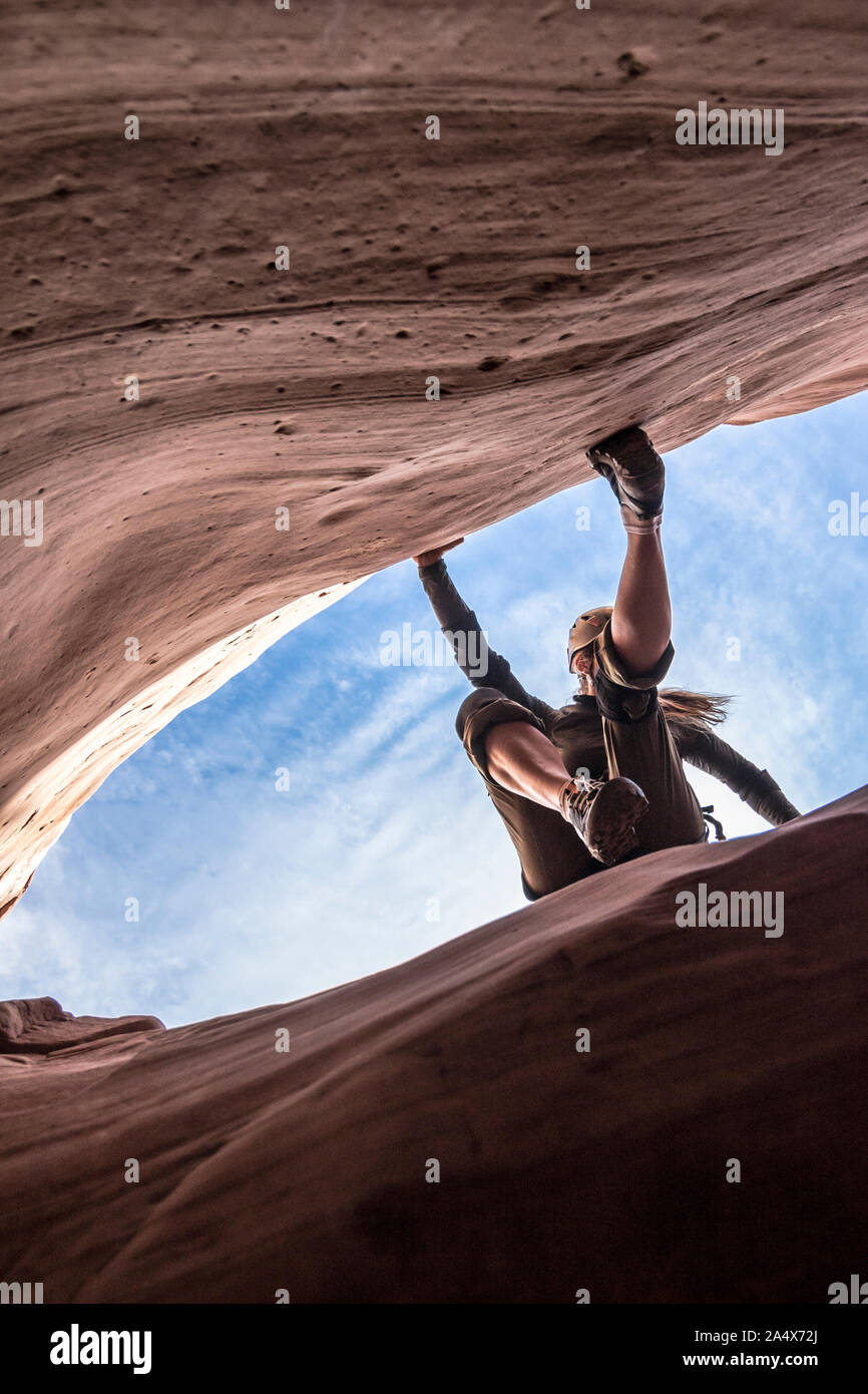 A woman canyoneer starts an exposed downclimb on slick sandstone walls Stock Photo