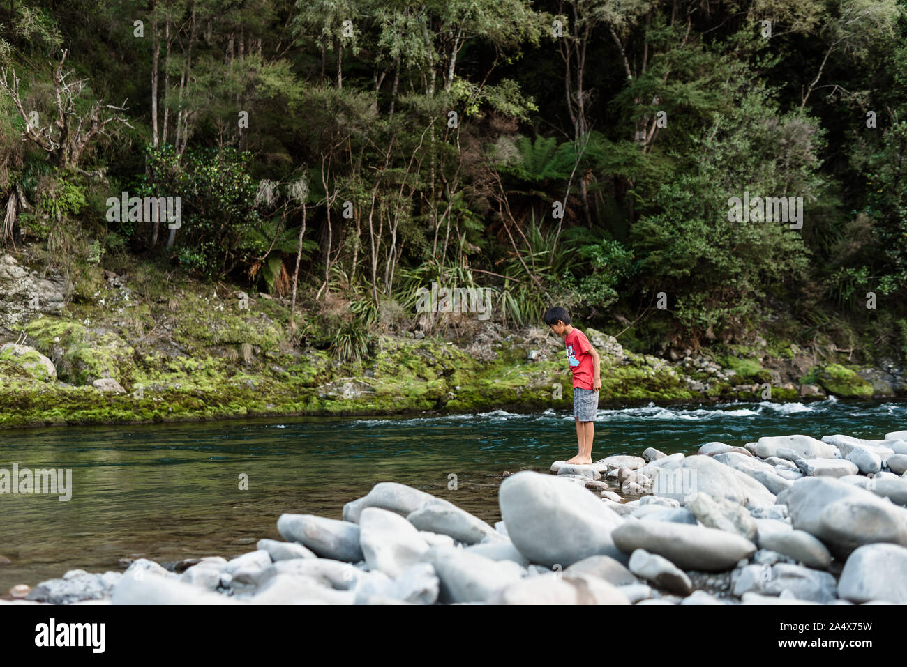Tween boy looking in water at the edge of a river Stock Photo
