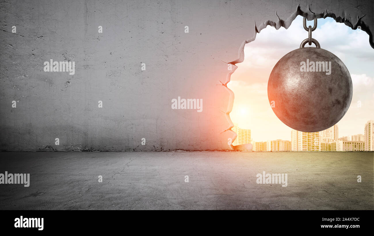A black wrecking ball hanging inside the opening in a concrete wall showing city landscape. Stock Photo
