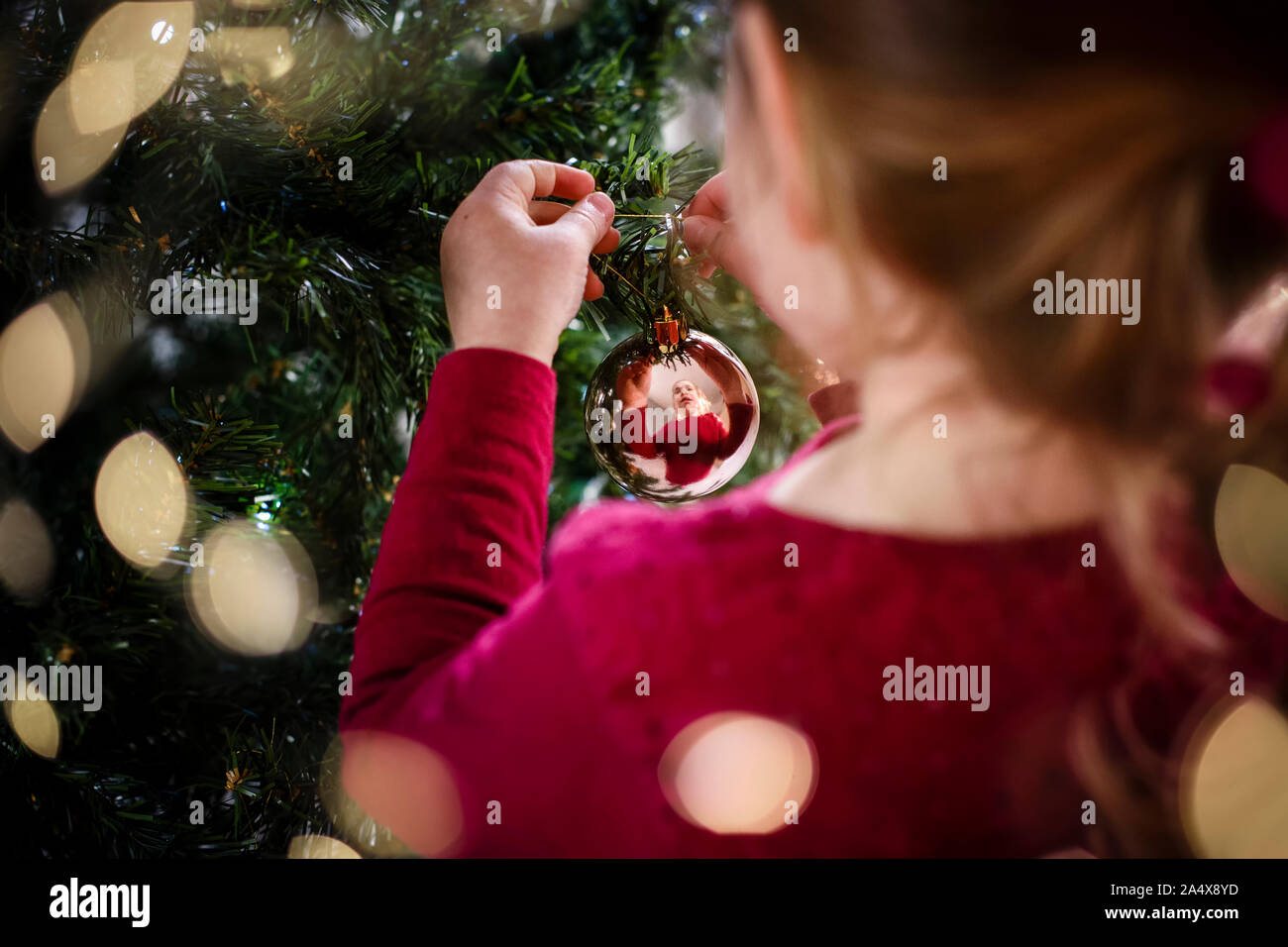 Festive image of girl decorating Christmas tree reflection in bauble Stock Photo