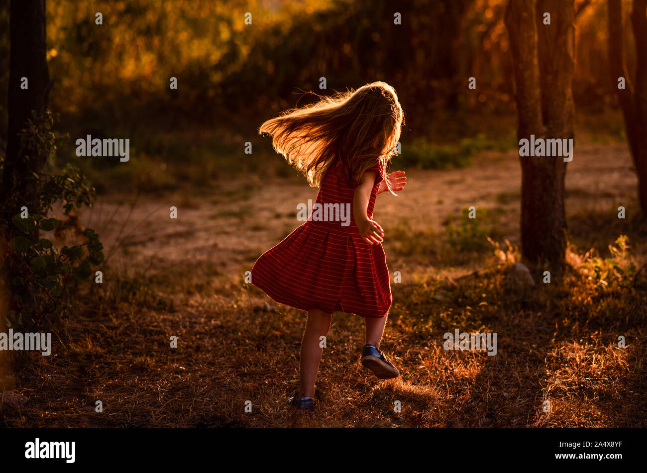 Girl runs through trees with light behind her Stock Photo