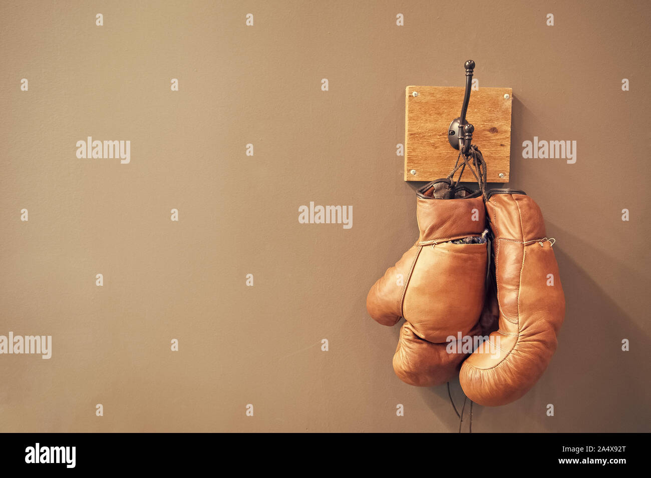 Museum of box sport. Box exhibition retro attributes. Boxing school. Vintage boxing gloves hang on hook wall background. Boxing gloves and copy space on grey. Finished boxing career famous sportsman. Stock Photo