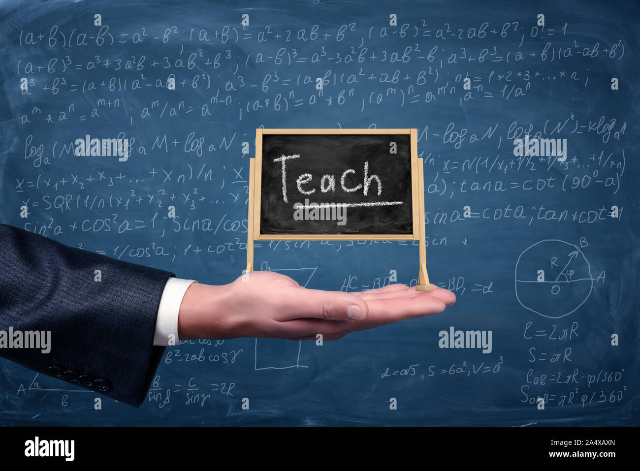 A businessman's hand holds a small easel blackboard with a word Teach on it with equations on the background. Stock Photo