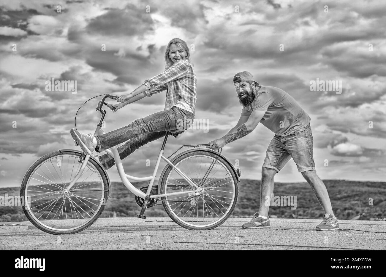 Woman rides bicycle sky background. Man helps keep balance and ride
