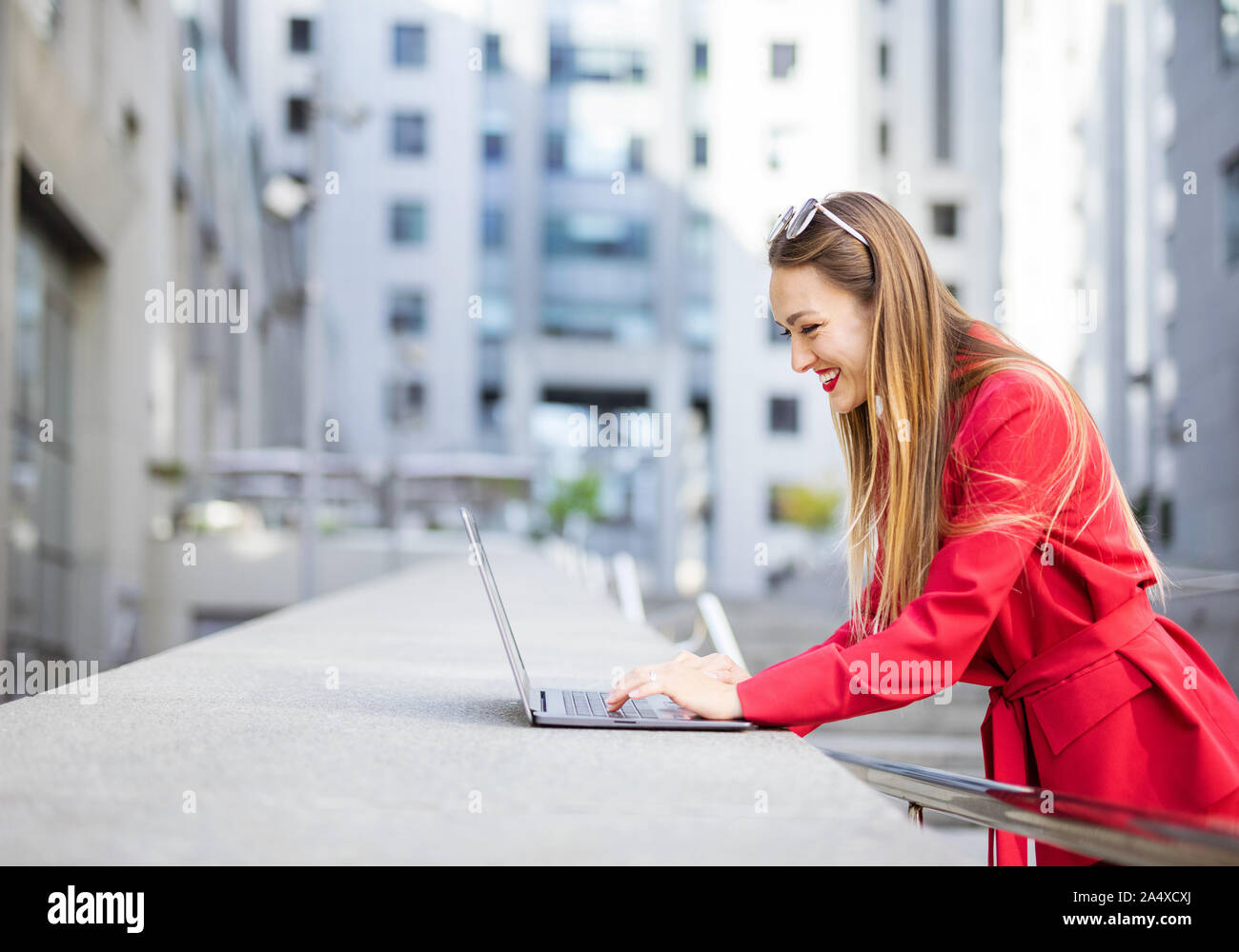 Attractive young woman using laptop outdoors in front of office buildings Stock Photo