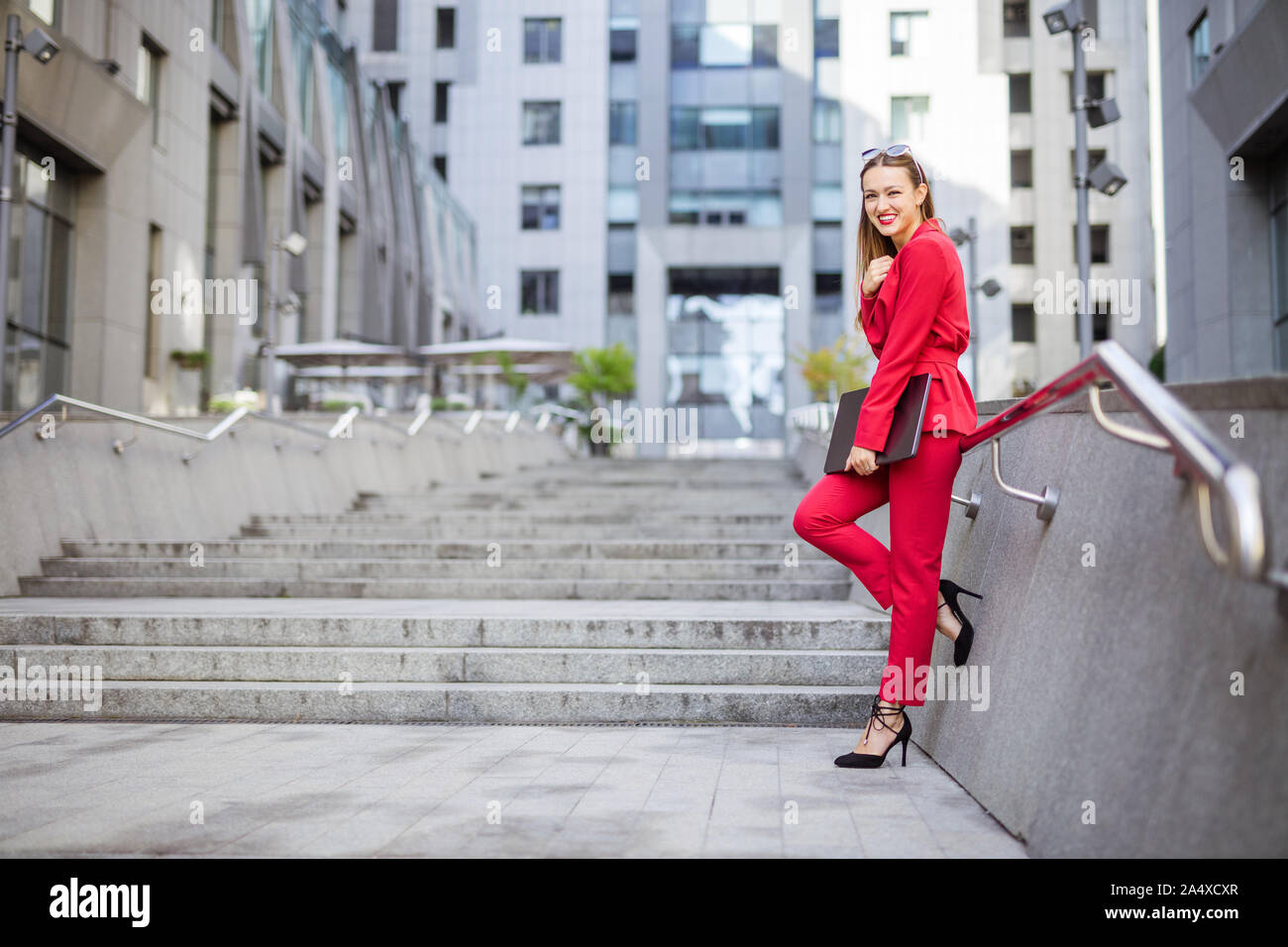 Attractive young woman with laptop standing on stairs in business district Stock Photo