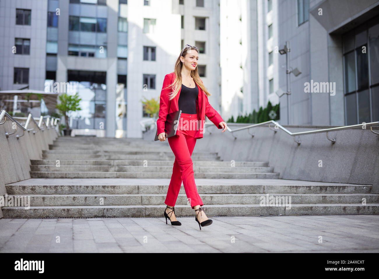 Attractive young woman with laptop walking outdoors in business district Stock Photo