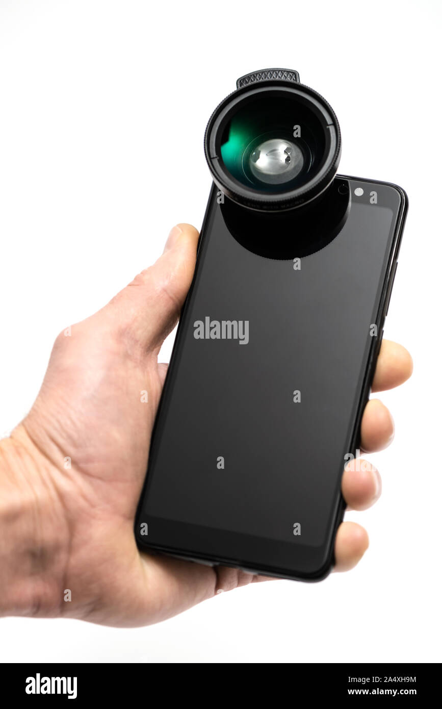 The human hand is holding a smartphone with an attached external lens. Stock Photo