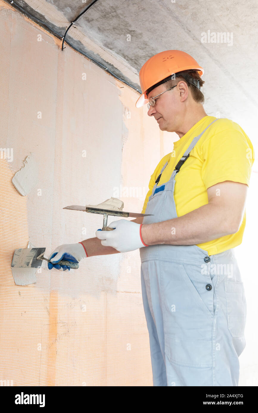 The worker is applying putty on a fiberglass mesh on the wall. He is using a trowel. Stock Photo