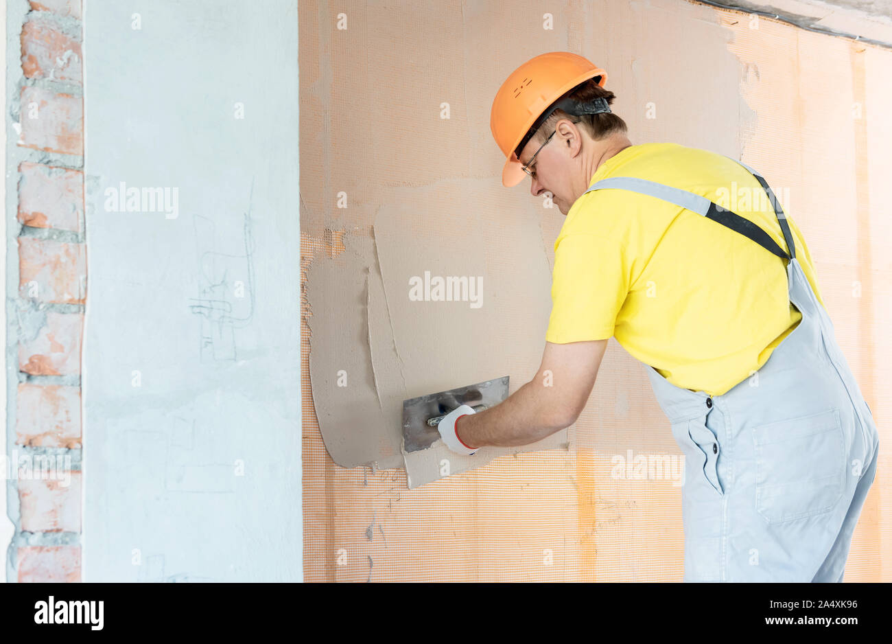 The worker is applying putty on a fiberglass mesh on the wall. He is using a trowel. Stock Photo