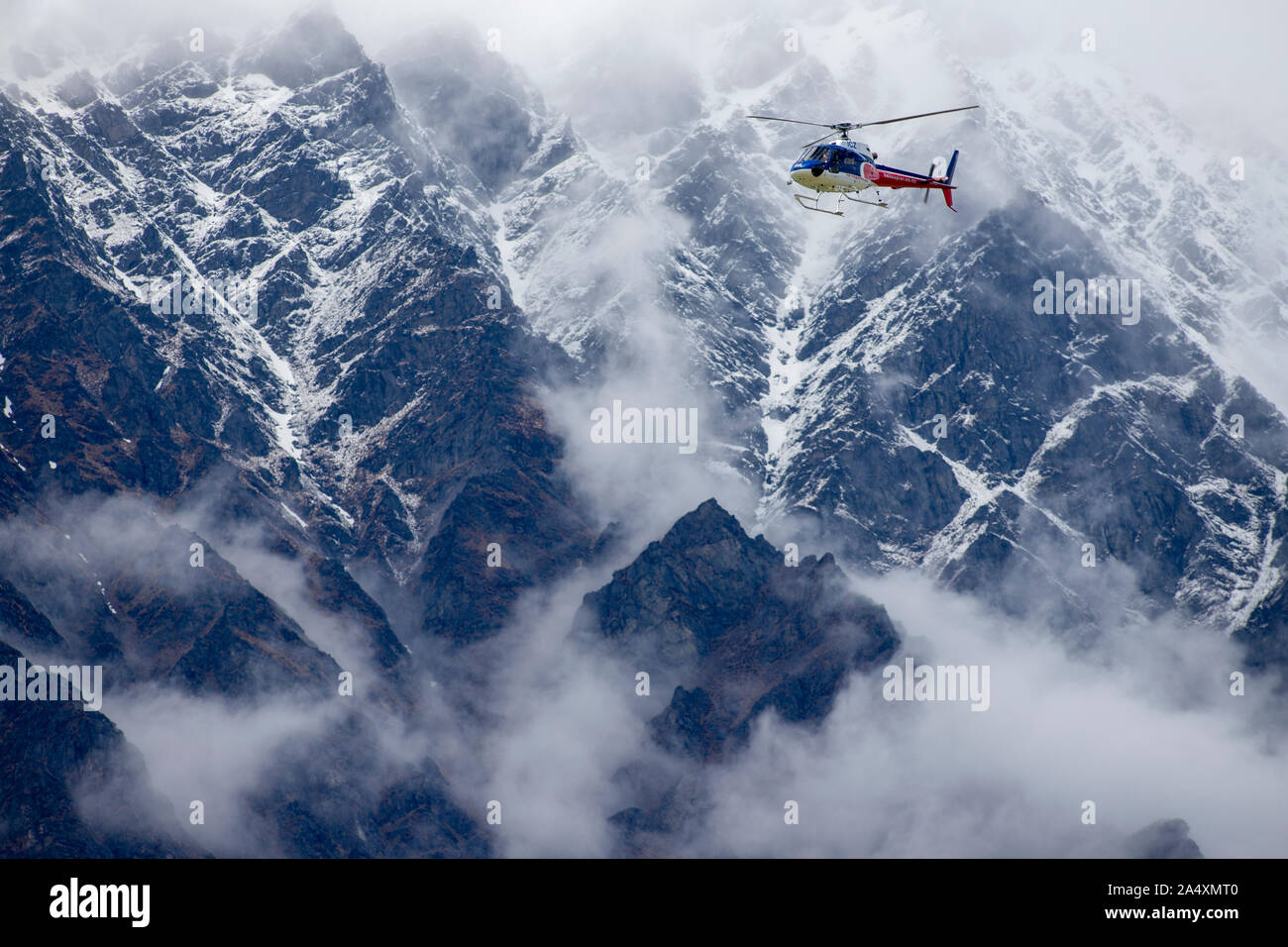 A helicopter leaves Queenstown Airport with the Remarkables range in the background, New Zealand Stock Photo