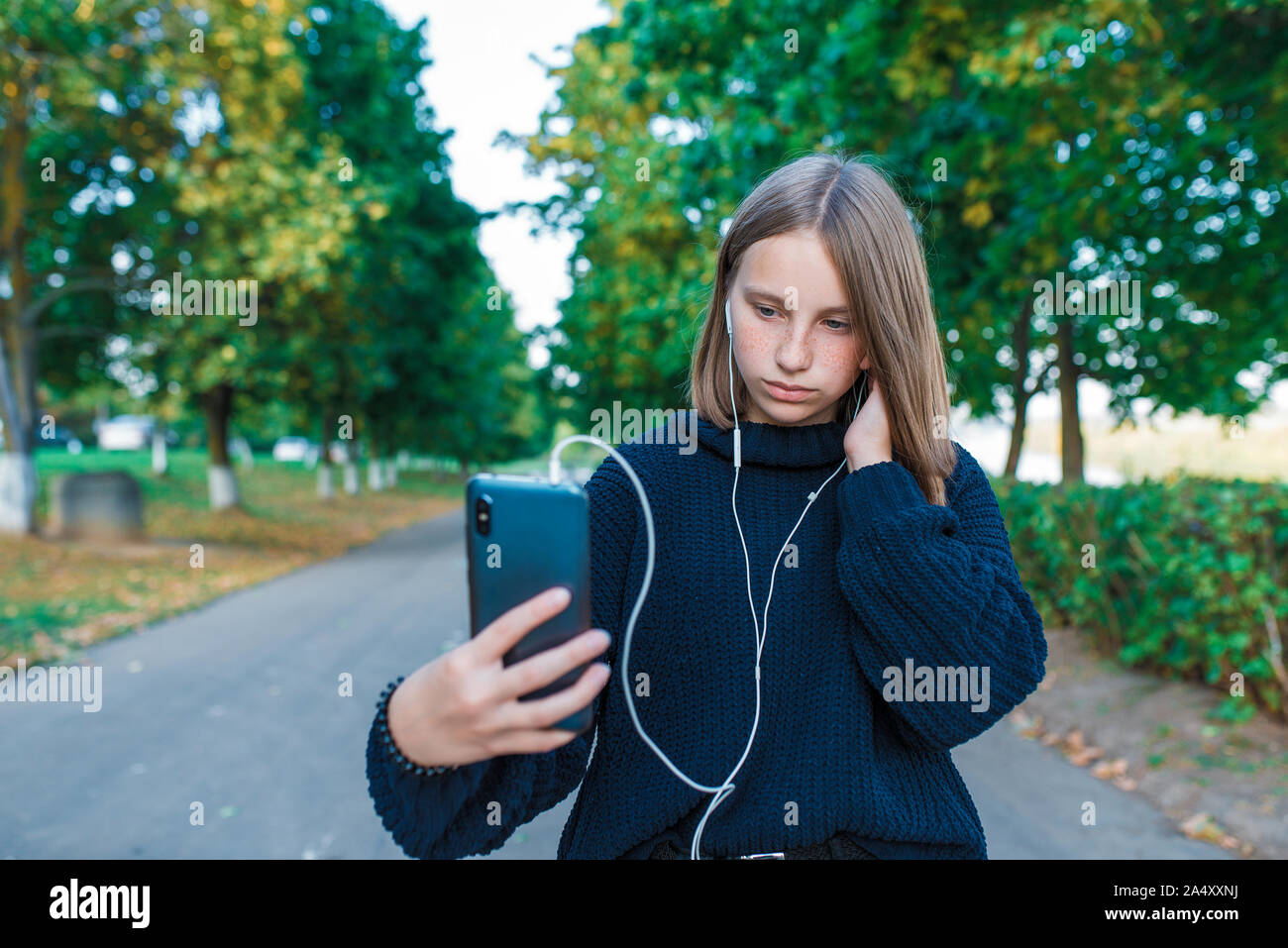teenage girl schoolgirl, teenager with headphones taking photos themselves phone, serious girl listens conversation, recording, video call, autumn Stock Photo