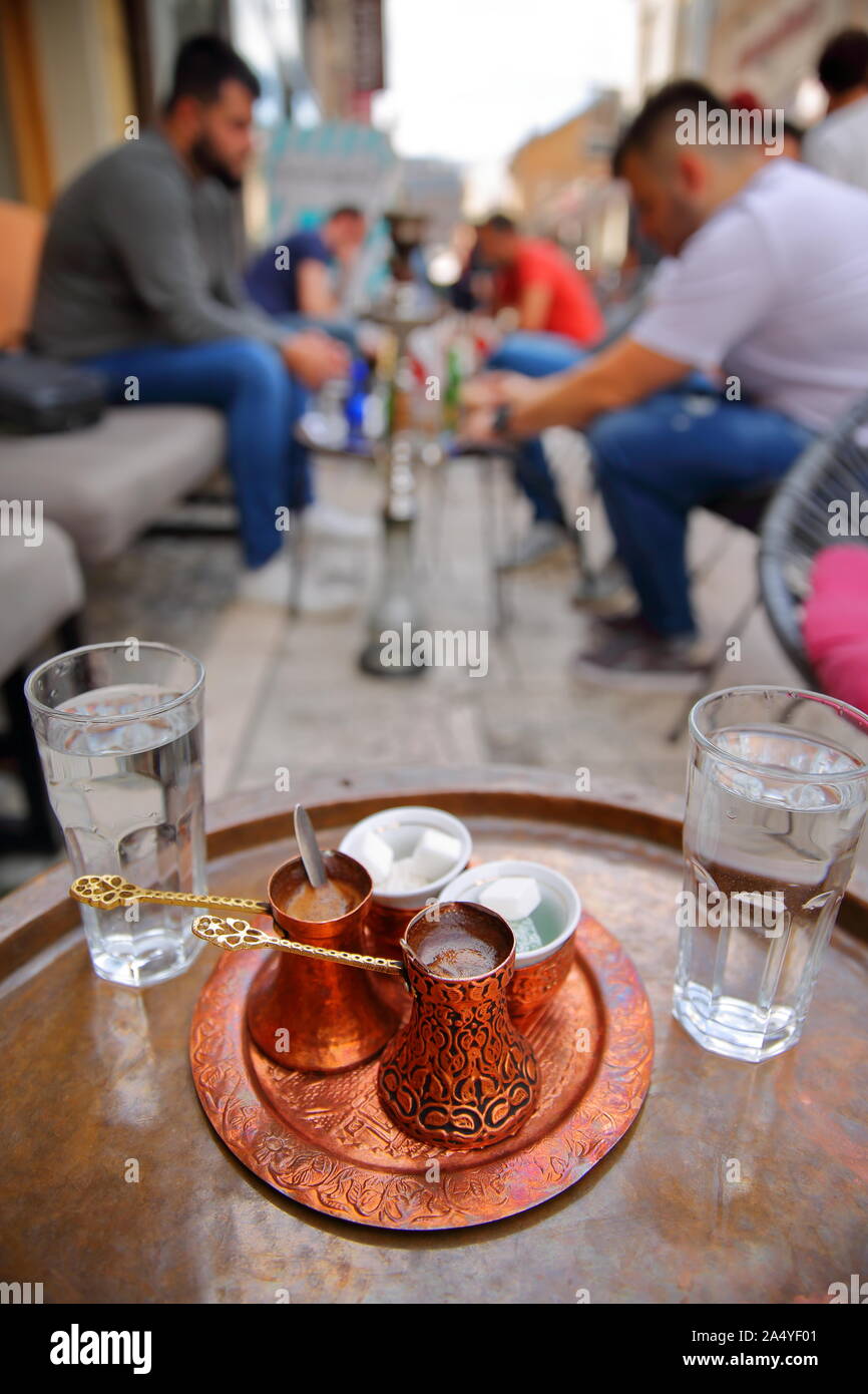 bosnia coffee cigarette Traditional Bosnian coffee cups (with a copper tray) with young people  smoking Shisha (or Hookah) in the background, Sarajevo, Bosnia and  Herzegovina Stock Photo