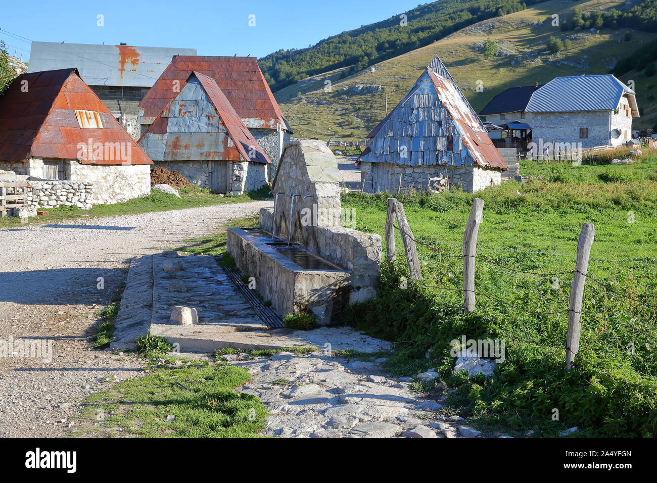Traditional houses in Lukomir village, with a fountain in the foreground, Bosnia and Herzegovina Stock Photo