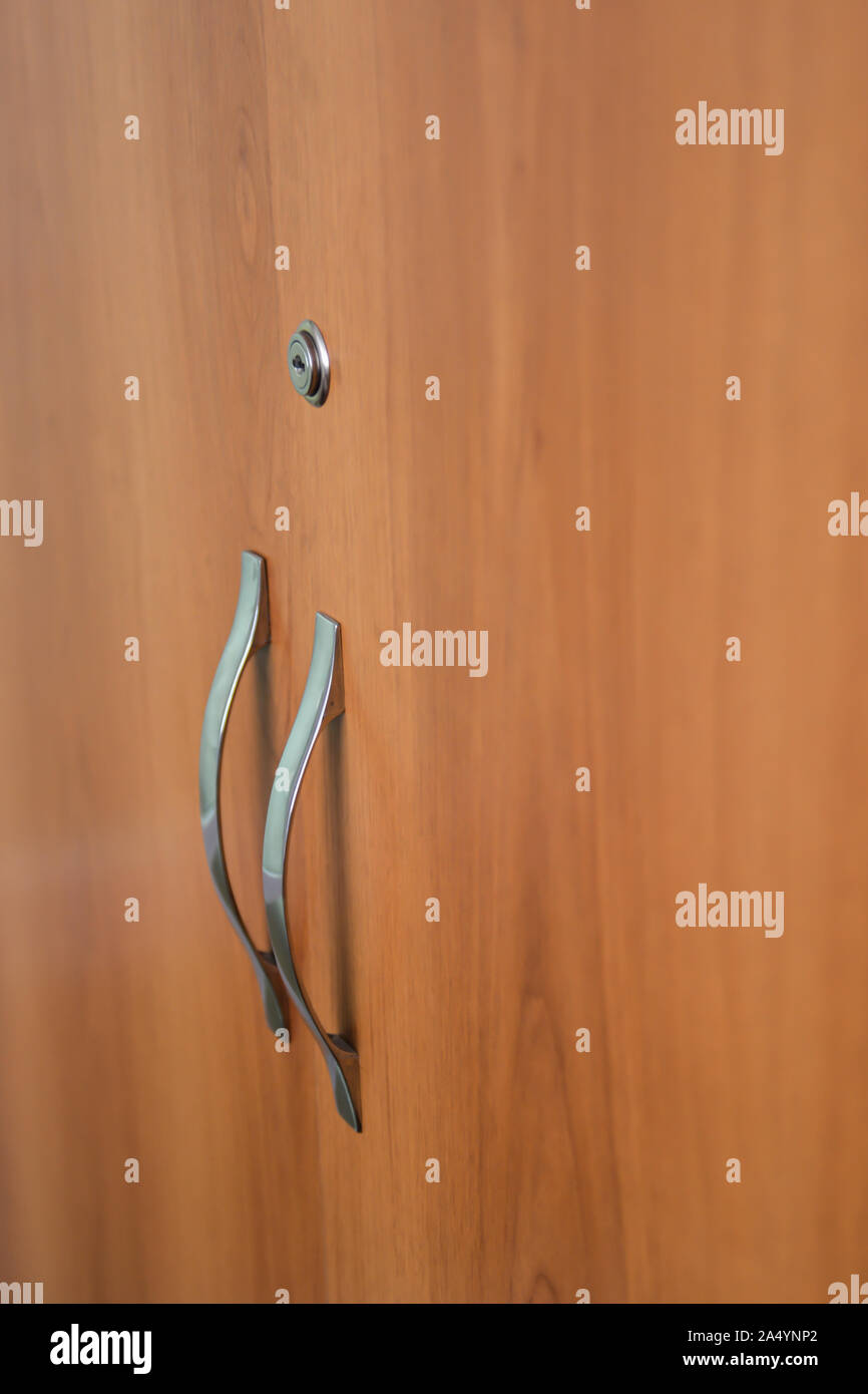Beautiful doors of cupboard with keyhole and door handle from brass close-up. Background image of wooden doors of locker. Stock Photo