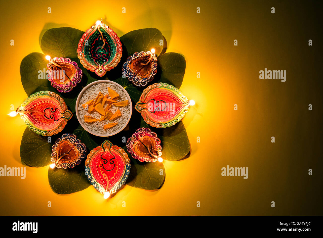 Happy Dussehra. Clay Diya lamps lit during Dussehra with yellow flowers, green leaf and rice on yellow pastel background. Dussehra Indian Festival con Stock Photo