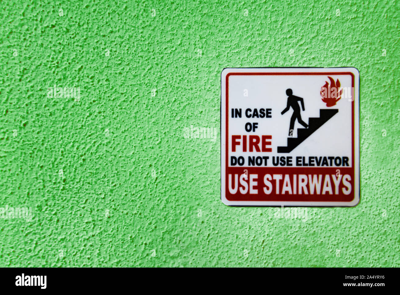 Red, black and white caution sign with person running from fire by stairs and warning not to use elevator in case of fire and to use stairs instead. S Stock Photo