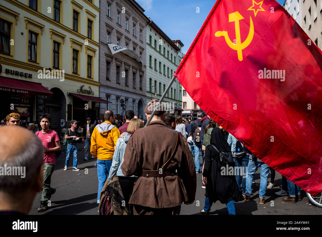 An elderly man in military uniform carries a communist flag on May Day 2019 in Berlin, Germany Stock Photo