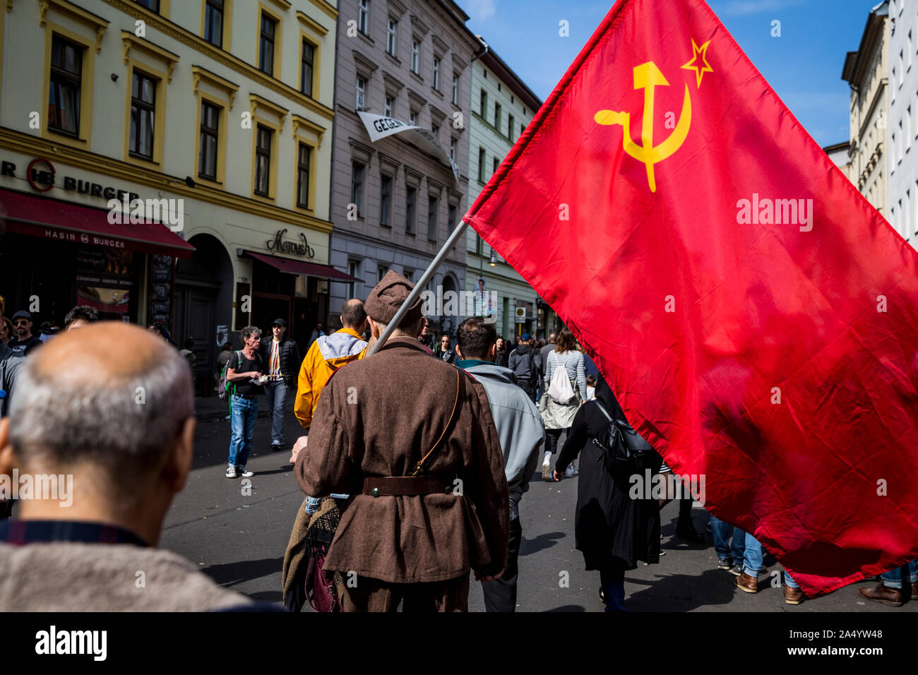 An elderly man in military uniform carries a communist flag on May Day 2019 in Berlin, Germany Stock Photo