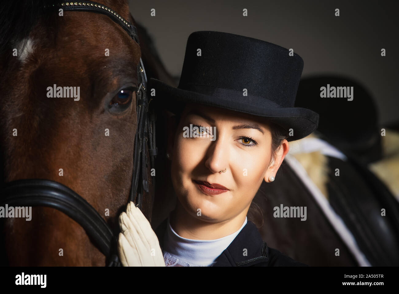 Young woman in tails in portraits next to her horse. She is holding her head next to the one of the horse and is looking into the camera. Stock Photo