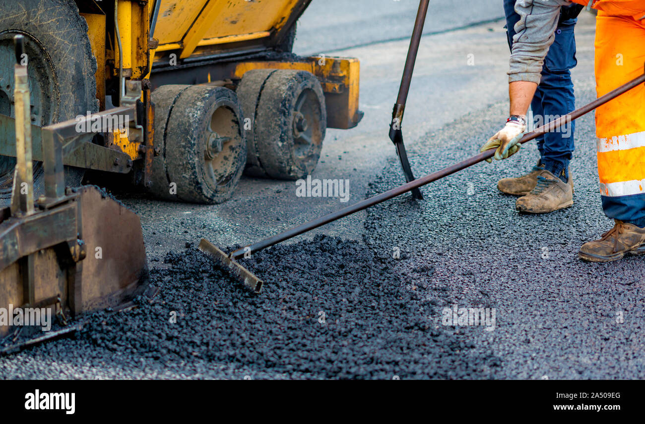 Worker regulate tracked paver laying asphalt heated to temperatures above 160 ° pavement on a runway Stock Photo