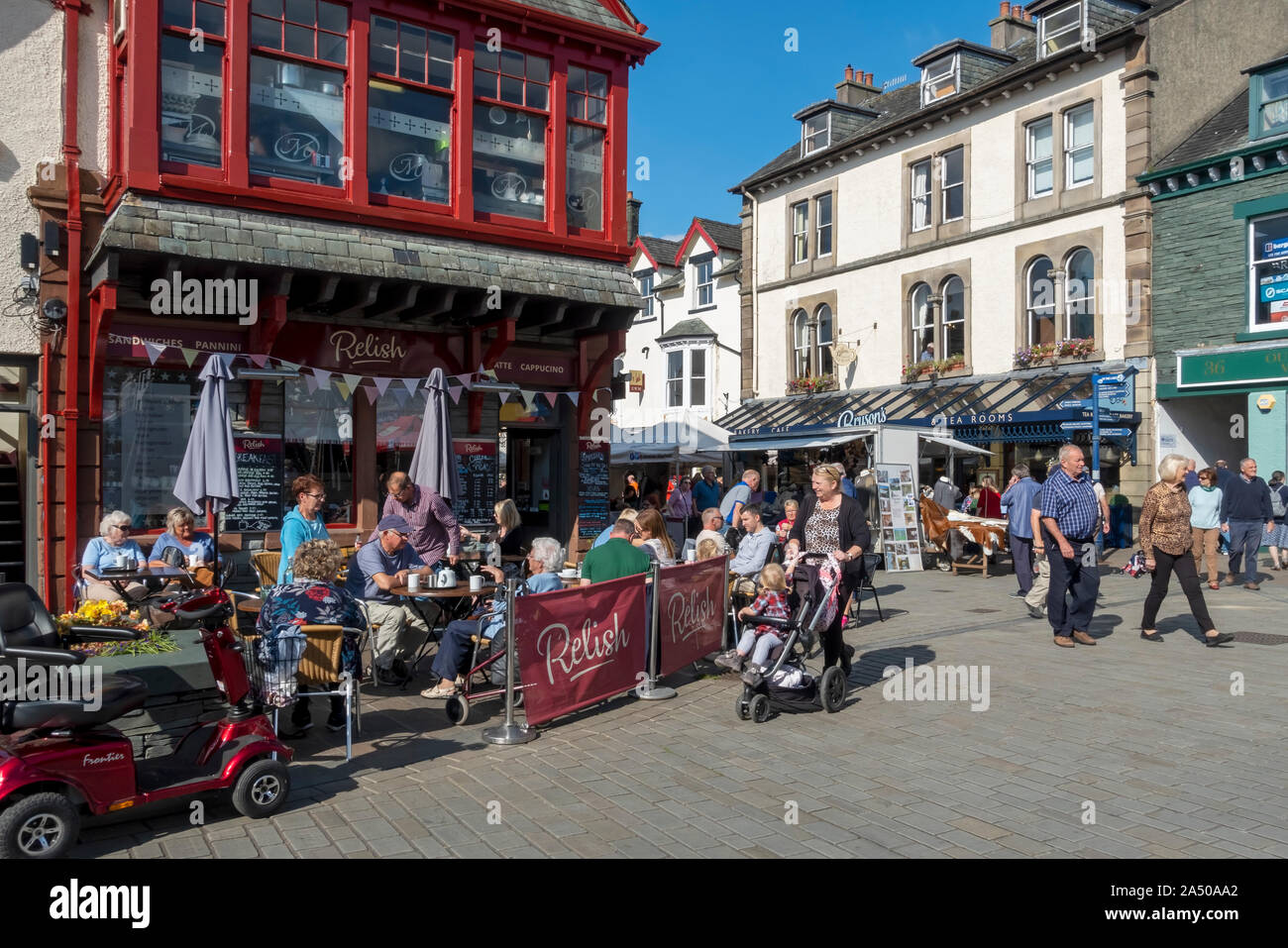 People tourists visitors sitting sat outside cafe eating and drinking in summer Market Square Keswick Cumbria England UK United Kingdom Great Britain Stock Photo