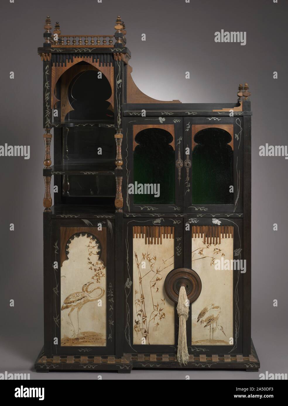 Cabinet, c. 1895. This cabinet is typical Bugatti. In form it is asymmetrical, with a towerlike element at one side. There are Islamic-inspired ornaments in its design, notably the onion-shaped arches in the upper stage. Japanese influence is evident in the white metal inlays and, even more clearly, in the sepia-painted parchment panels in the lower portion of the cabinet. One of these, at the bottom left, is signed &quot;Casati.&quot; No contemporary painter with this name has been discovered, but the Marchesa Luisa Casati, a well-known socialite in Milan, is known to have been an acquaintanc Stock Photo