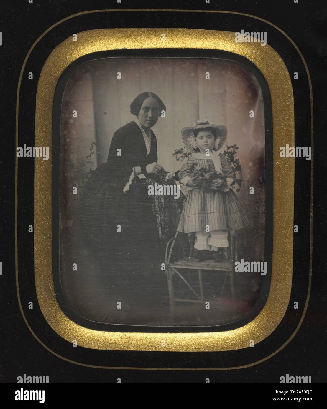 Child Standing on a Chair Holding Flowers, with Mother, c. 1855. Until the mid-1850s the daguerreotype process was the method preferred by the commercial photographers willing to meet the ever-growing demand for likenesses of family and friends. This daguerreotype captures the patience of a mother and child, who were required to hold their poses for some time during the exposure of the silver-coated copper plate. Only the bouquet of flowers held by the child is slightly blurred. Characteristic of the technique, the details in the image-fabric, facial features, and accessories-are clearly defin Stock Photo