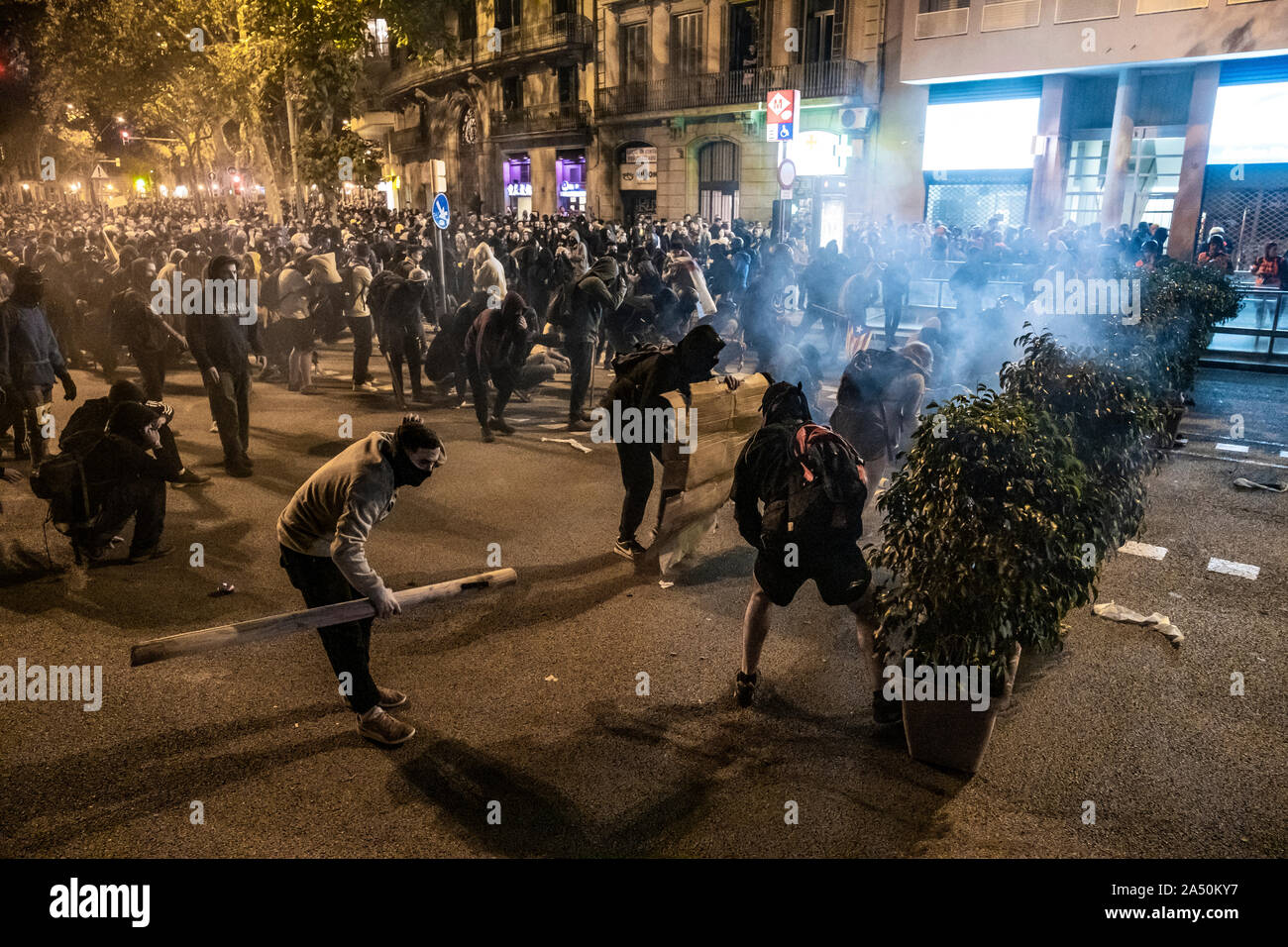 Protesters take cover amidst teargas smoke during the demonstration.Hundreds of protesters concentrated on the Gran Vía Street in Barcelona during the third day of protest following the sentences of the Spanish Supreme Court that condemns Catalan political prisoners to long prison terms. The demonstration culminated in front of the headquarters of the Department of Interior of the Generalitat with heavy police charges and barricades set on fire. Stock Photo