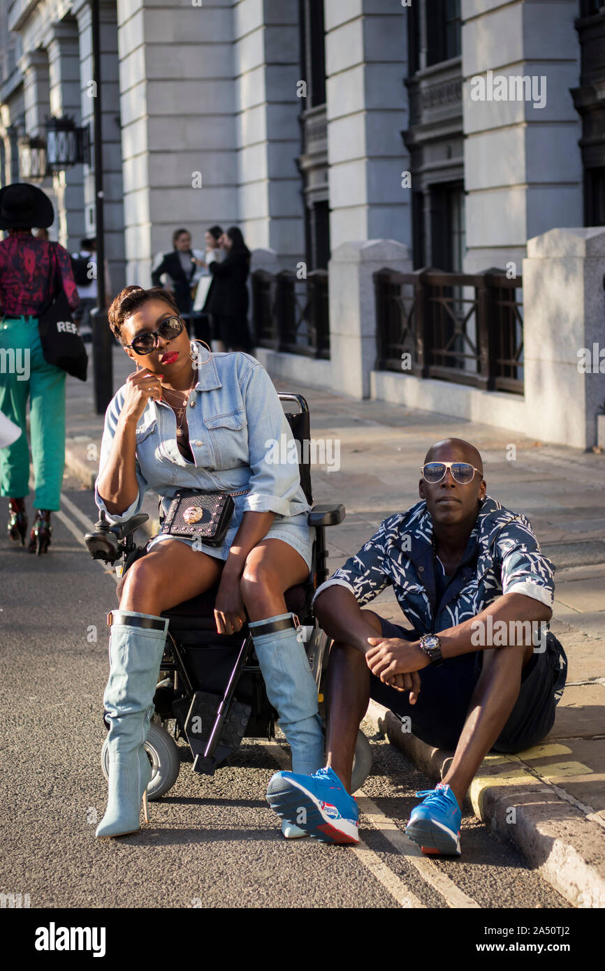 LONDON, UK- SEPTEMBER 13 2019: People on the street during the London Fashion Week. Girl in a denim shirt and a short leather skirt sits in a wheelcha Stock Photo