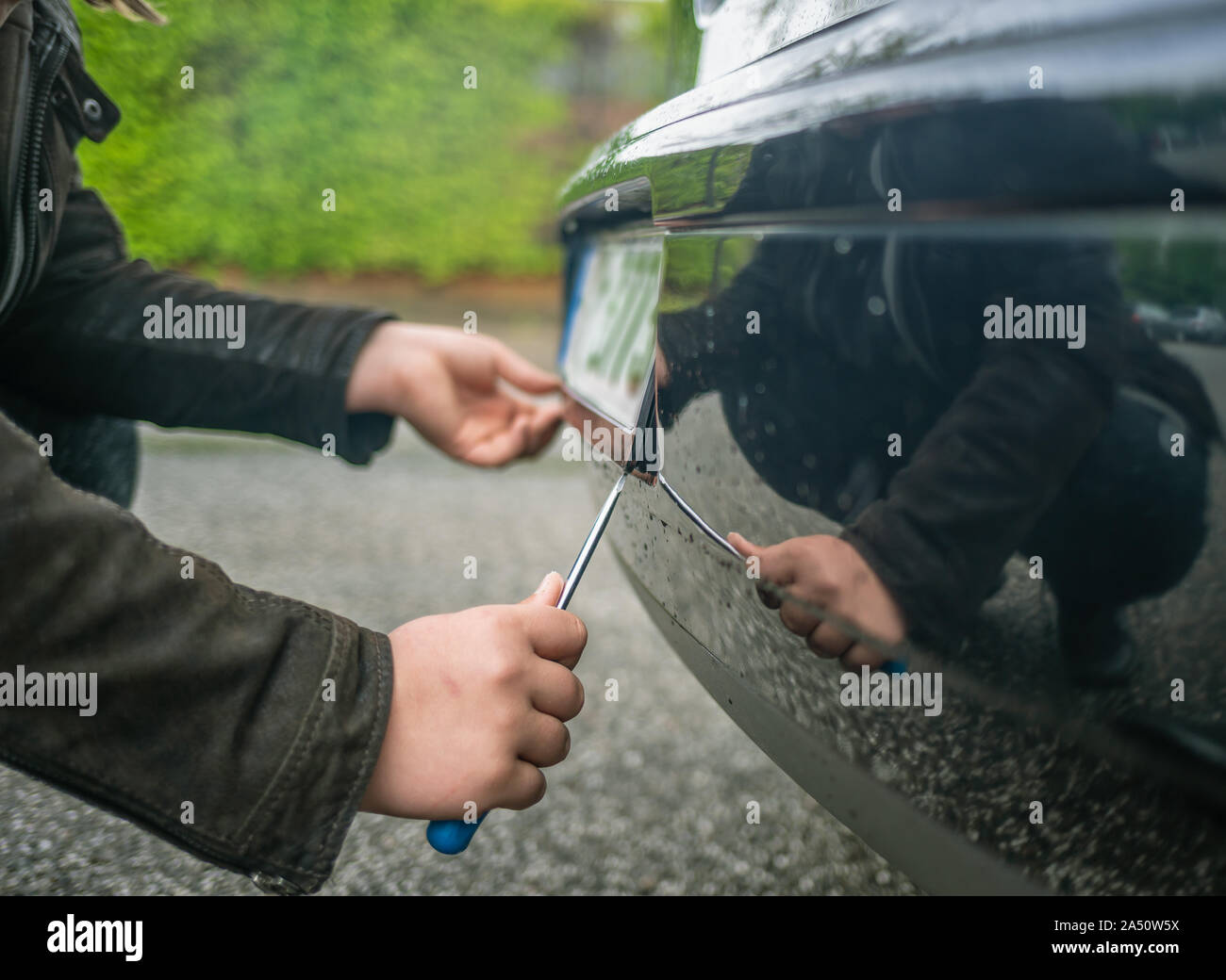 A person steals the license plate on a car with a screwdriver Stock